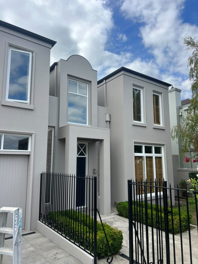 Rendered Kew house exterior in light grey with white window frames behind a black iron fence